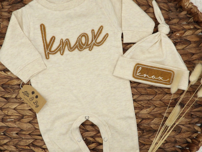 May include: A beige baby onesie with long sleeves and a brown felt appliqu&eacute; that says "knox". A matching beige beanie with a brown felt appliqu&eacute; that says "knox" is also included.