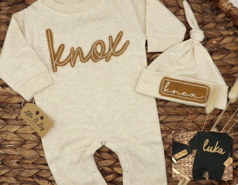 May include: A beige baby onesie with the name "Knox" embroidered in brown thread. A matching beige hat with a brown patch that says "Knox" is also included. The onesie and hat are on a woven brown background.
