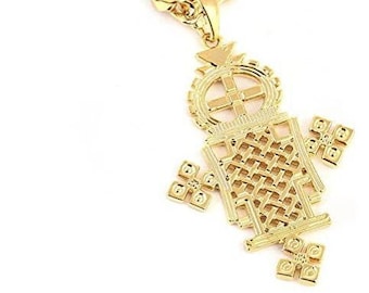 May include: A gold chain necklace with a large, intricate gold pendant in the shape of a cross. The pendant has a woven design and is detailed with small squares.