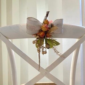May include: A white chair with a woven seat and a decorative bow with berries and greenery on the back.