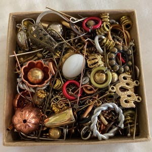 May include: A box filled with a variety of jewelry making supplies, including beads, charms, findings, and wire. The box is overflowing with a mix of gold, silver, copper, and red colored pieces.