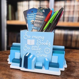 Puede incluir: Organizador de escritorio azul y blanco con forma de pila de libros con el texto "So many Books So little Time".