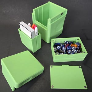 May include: A light green modular gaming storage system consisting of a tall open container, a smaller card holder with white and orange markers, a rectangular box filled with blue and white dice, and two flat lids with visible magnetic closures.