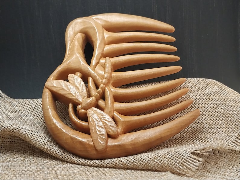 Puede incluir: Un peine de madera con un dise&ntilde;o de lib&eacute;lula tallado. El peine tiene siete dientes y est&aacute; hecho de madera marr&oacute;n claro.