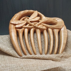 Puede incluir: Un peine de madera con un dise&ntilde;o de lib&eacute;lula tallado. El peine est&aacute; hecho de madera marr&oacute;n claro y tiene un acabado natural. La lib&eacute;lula est&aacute; tallada en detalle y tiene una apariencia realista.