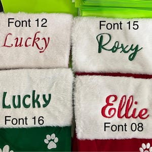 May include: Four Christmas stockings with white faux fur cuffs and colorful embroidered names: "Lucky" in red, "Roxy" in green, "Lucky" in green, and "Ellie" in red. The stockings have green and red bases with paw print details.