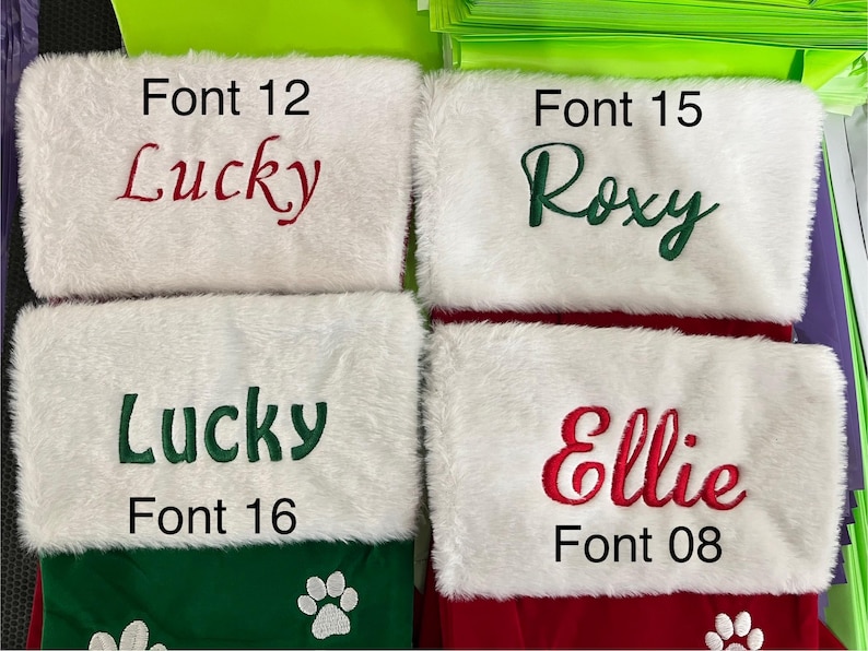 May include: Four Christmas stockings with white faux fur cuffs and colorful embroidered names: "Lucky" in red, "Roxy" in green, "Lucky" in green, and "Ellie" in red. The stockings have green and red bases with paw print details.