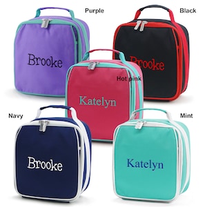 May include: Five personalized lunch bags in various colors: purple, black, hot pink, navy, and mint. Each bag has a top handle, a zipper closure, and a name embroidered on the front. The bags have contrasting trim.