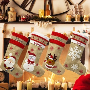 May include: Four personalized Christmas stockings with burlap fabric and red trim. The stockings are decorated with embroidered snowflakes, a snowman, a reindeer, and a Santa Claus. The stockings are labeled "Karen", "Chris", "Alex", and "Bella".