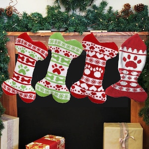 May include: Four Christmas stockings shaped like dog bones, in red, white, and green. Each stocking has a paw print or bone pattern. They are hanging above a fireplace, with garland and lights.