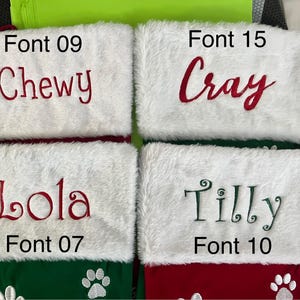 May include: Four Christmas stockings with white faux fur cuffs and red and green bodies. Each stocking has a name embroidered in a different font: "Chewy", "Cray", "Lola", and "Tilly". Paw prints decorate the bottom of the stockings.