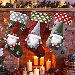 May include: Three personalized Christmas stockings with gnome faces and embroidered names: Laura, Karter, and Kathy. The stockings are red, green, and gray with white polka dots.