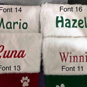 May include: Four personalized Christmas stockings with white faux fur tops. The names "Mario" in green, "Hazel" in green, "Luna" in red, and "Winnie" in red are embroidered on the stockings. The bottom sections are red and green with paw print designs.