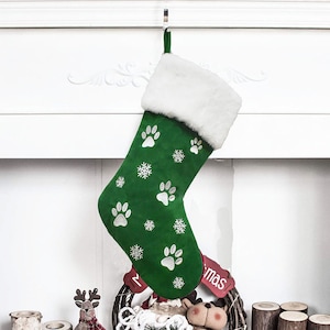 May include: A green Christmas stocking with white paw prints and snowflakes. The top of the stocking is trimmed with white faux fur. A red tag with the word "mas" is visible.