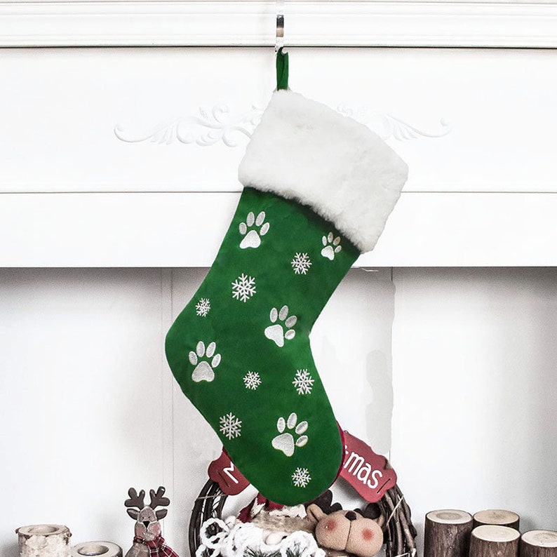 May include: A green Christmas stocking with white paw prints and snowflakes. The top of the stocking is trimmed with white faux fur. A red tag with the word "mas" is visible.