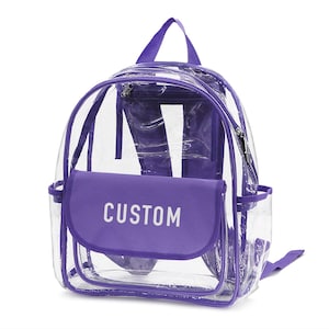 May include: Clear backpack with purple trim and accents. Features a front flap with the word "CUSTOM" in white. Includes a top handle, adjustable straps, and a zippered main compartment. Perfect for school or events.