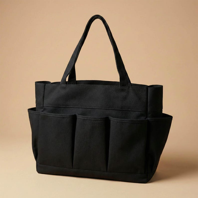 May include: Black tote bag with multiple exterior pockets and two sturdy handles. The bag is made of a durable fabric and features a rectangular shape with a flat bottom. The pockets are evenly spaced along the sides.