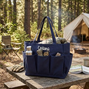 May include: A navy blue tote bag with multiple exterior pockets, filled with items like a water bottle, gloves, and a compass. The bag has the name "Collins" embroidered in white. The scene is set outdoors with a tent and campfire in the background.