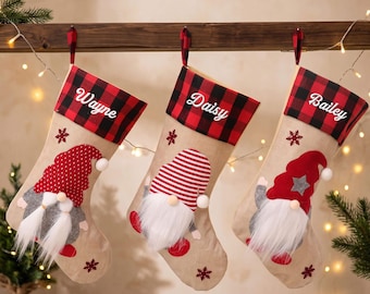 May include: Three beige Christmas stockings featuring a red and black buffalo plaid cuff with the names Wayne, Daisy, and Bailey embroidered in white. Each stocking displays a gnome with a white beard and a unique red hat, accented by snowflakes.