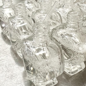 May include: A group of clear glass bottles with intricate designs. The bottles are arranged in a row, and one bottle is being filled with liquid from a clear dropper.