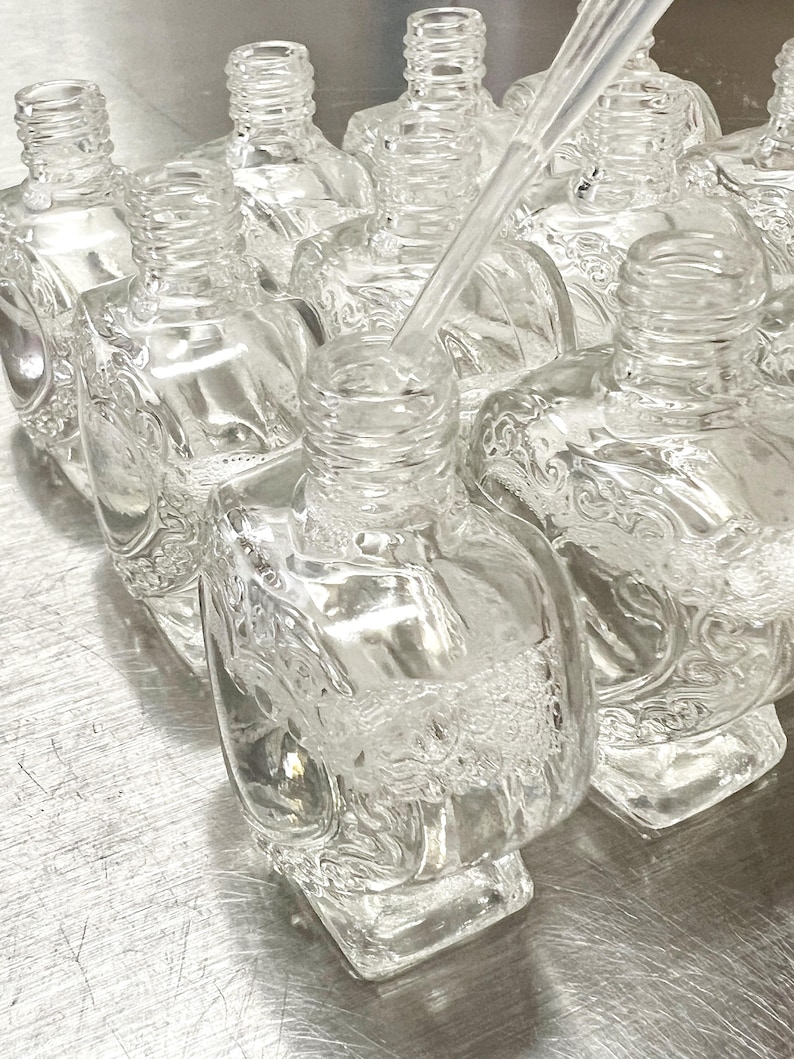 May include: A group of clear glass bottles with intricate designs. The bottles are arranged in a row, and one bottle is being filled with liquid from a clear dropper.
