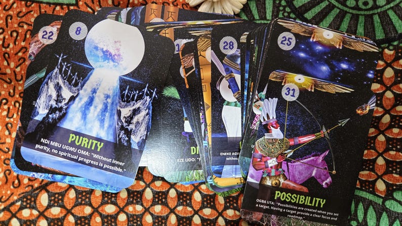 May include: A deck of oracle cards with colorful illustrations and text. The cards feature images of a waterfall, a figure with a bow and arrow, and other symbolic designs. The word "Purity" and "Possibility" are visible on the cards.