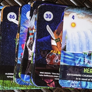 May include: A collection of oracle cards with colorful illustrations and text. Each card features a unique image, number, and text, with themes of healing and spirituality. The cards have a dark blue background with various images and text.