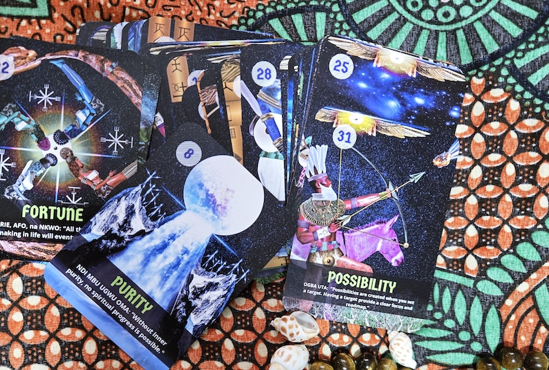 May include: A collection of oracle cards with celestial and mythological imagery. The cards feature illustrations of figures, celestial bodies, and text such as "Fortune," "Purity," and "Possibility." The cards are on a patterned fabric.