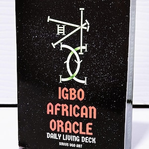 May include: A black box featuring the text "IGBO AFRICAN ORACLE DAILY LIVING DECK" in orange and white. The box has a green and white abstract design. The product is by Sirius Ugo Art.