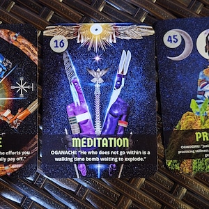 May include: Three tarot cards with vibrant illustrations and text. The cards feature the words "FORTUNE", "MEDITATION", and "PROTECTION". Each card has a unique design with figures and symbols against a dark, starry background. The cards are displayed on a textured surface.
