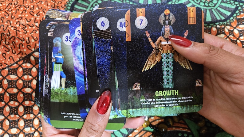 May include: A deck of tarot cards featuring colorful illustrations and numbers. One card displays the word "GROWTH" with an image of a woman with wings. Other cards show figures and celestial designs. The cards are held in a person's hand.