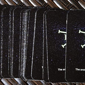 May include: A deck of black cards with a starry background. Each card features the word "IGBO" and a geometric design in white and green. The text "The answers are within you" is printed on the bottom of the cards.