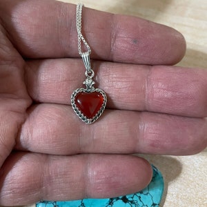May include: A silver heart-shaped pendant necklace with a red carnelian stone. The necklace is on a silver chain.