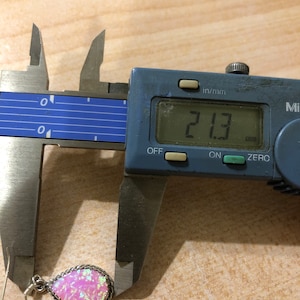 May include: A pink opal earring with a silver setting, measured at 2.13 mm using a digital caliper.