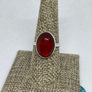 May include: A silver ring with a large, oval-shaped, red carnelian gemstone.