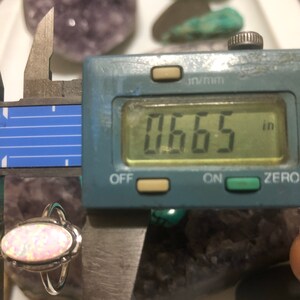 May include: A silver ring with a pink opal stone. The ring is measured with a caliper, showing a measurement of 0.665 inches.