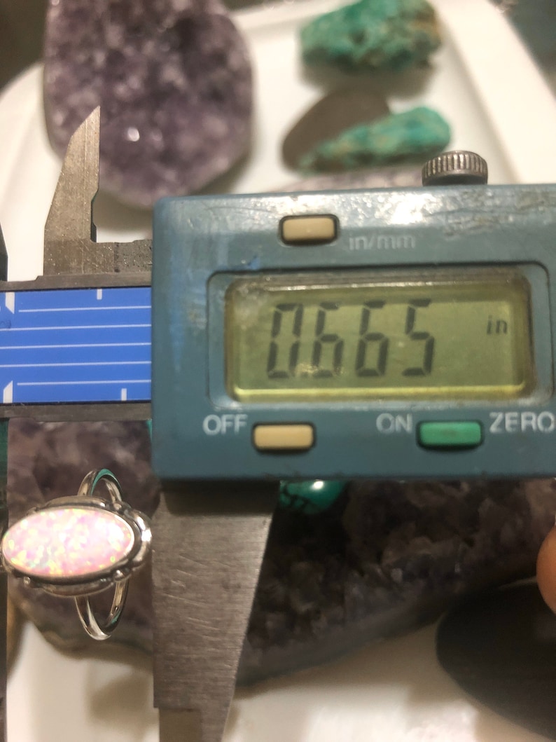May include: A silver ring with a pink opal stone. The ring is measured with a caliper, showing a measurement of 0.665 inches.