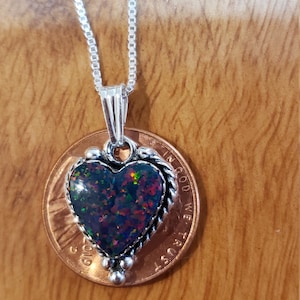 May include: A heart-shaped pendant necklace with a silver chain. The pendant features a dark opal with red, green, and blue flashes, set in a silver frame. The pendant is approximately 0.75 inches wide.