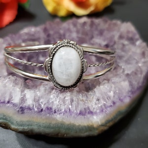 May include: A silver bracelet with a white oval gemstone set in a silver bezel. The bracelet has a twisted wire design.