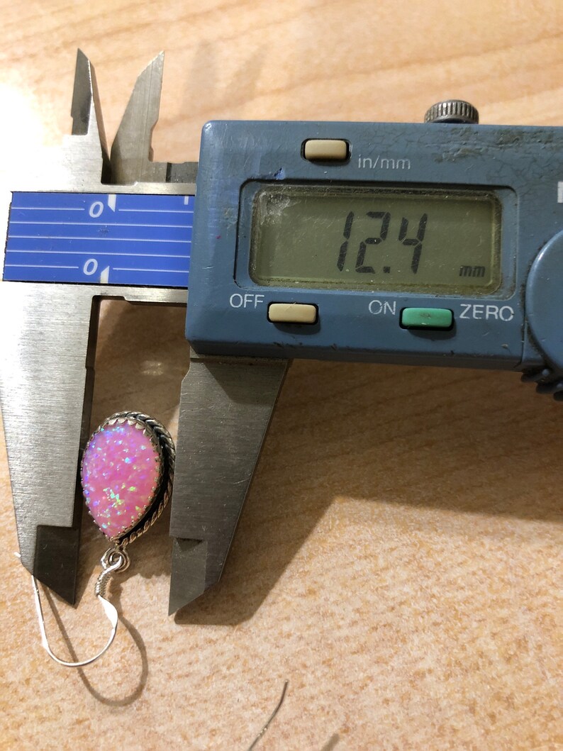 May include: A pink opal gemstone earring with a silver setting, measured at 12.4 mm in diameter using a digital caliper.