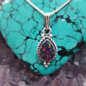May include: A silver chain necklace with a teardrop-shaped pendant featuring a dark iridescent opal stone set in a silver filigree design.