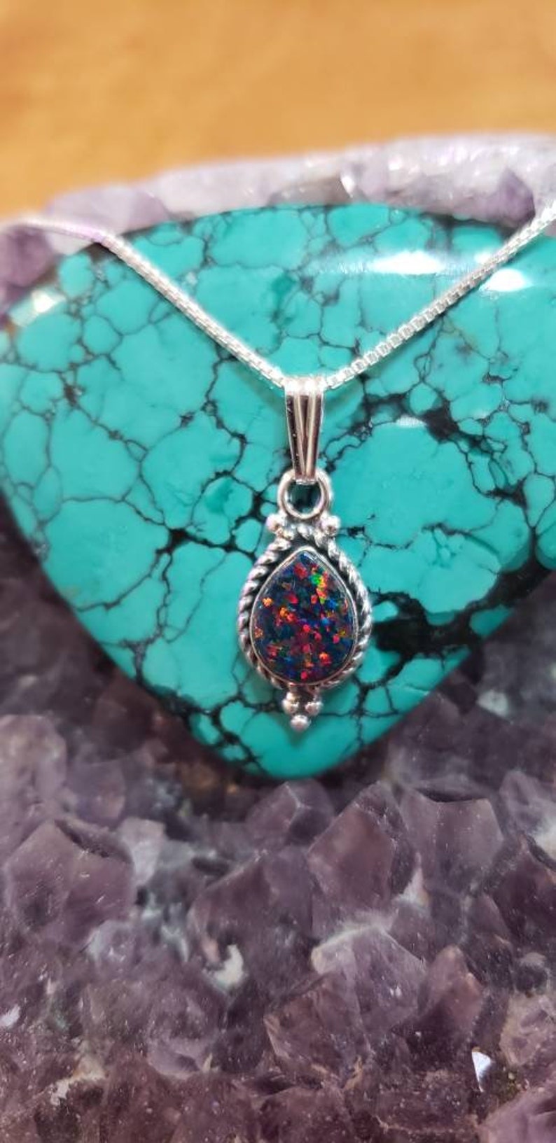 May include: A silver chain necklace with a teardrop-shaped pendant featuring a dark iridescent opal stone set in a silver filigree design.