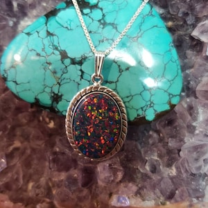Puede incluir: Un collar de cadena de plata con un colgante de forma ovalada que presenta una opala iridiscente oscura engastada en un bisel de plata.