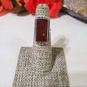 May include: A silver ring with a rectangular, reddish-brown gemstone set in a decorative border.
