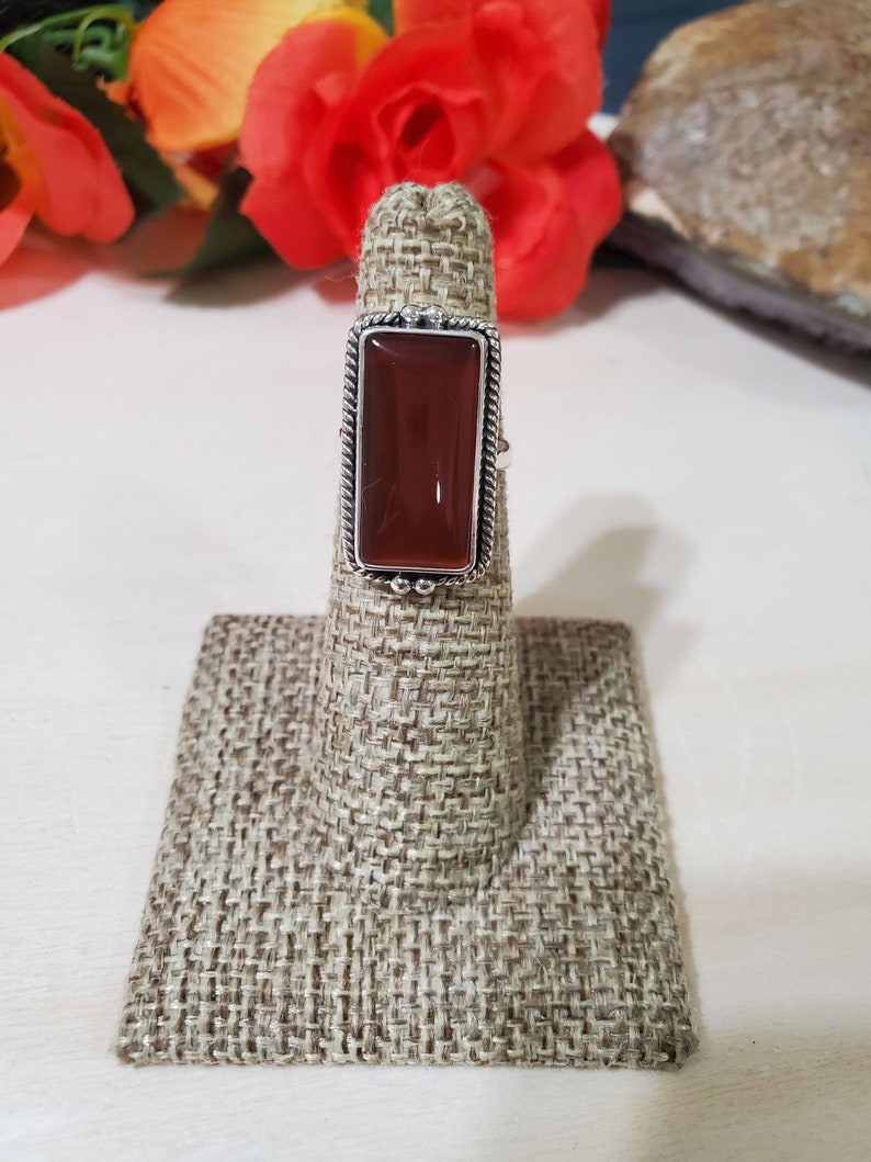 May include: A silver ring with a rectangular, reddish-brown gemstone set in a decorative border.