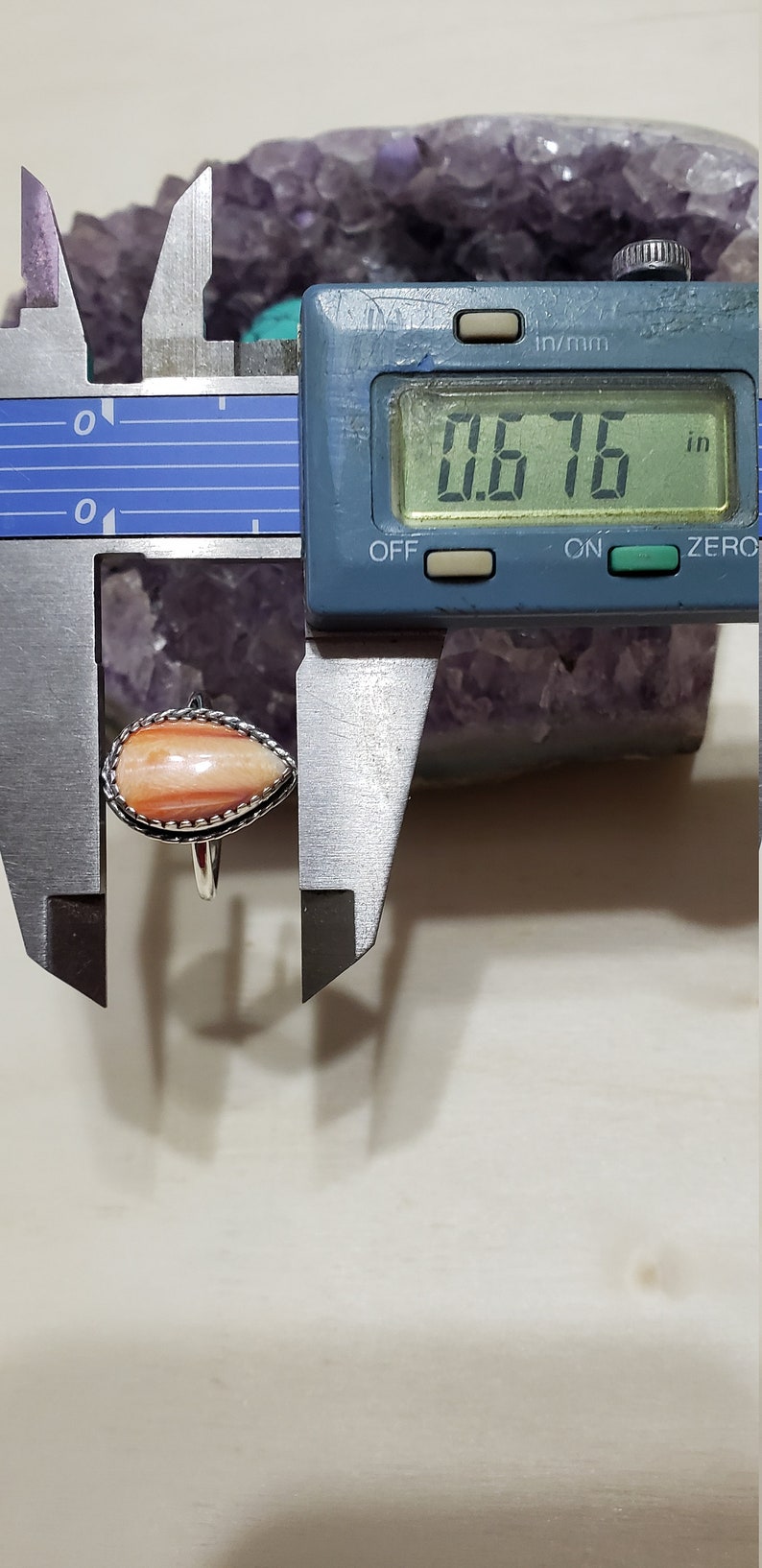 May include: A close-up of a ring with a teardrop-shaped, orange and white stone. The stone is 0.676 inches wide. The ring is set in silver.
