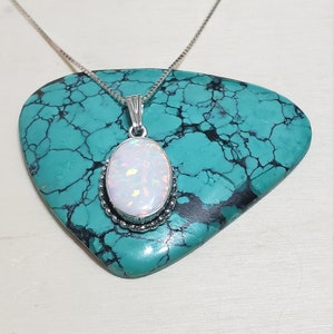 May include: A silver chain necklace with a white opal pendant set in a silver bezel. The pendant is oval shaped and has a delicate silver border.