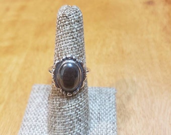 Puede incluir: Un anillo de plata con una piedra ovalada negra engastada en un engaste de plata decorativo.