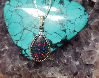 May include: A silver chain necklace with a teardrop-shaped opal pendant. The opal is a dark iridescent green, blue, and red color. The pendant is set in a silver bezel.