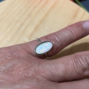 May include: A silver ring with an oval-shaped white opal gemstone. The ring has a delicate, twisted band.
